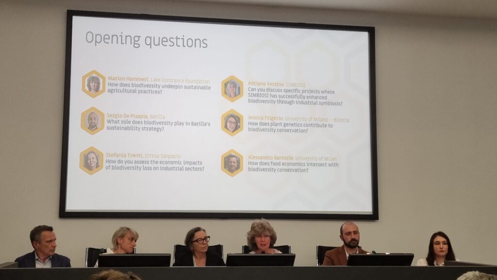 Zusehen sind die Teilnehmer*innen der Podiumsdiskussion. Sie sitzen auf Stühlen hinter einem langen Pult. Auf der Präsentation hinter ihnen sind "opening questions" dargestellt. Marion Hammerls Frage ist: "How does biodiversity underpin sustainable agricultural practices?"