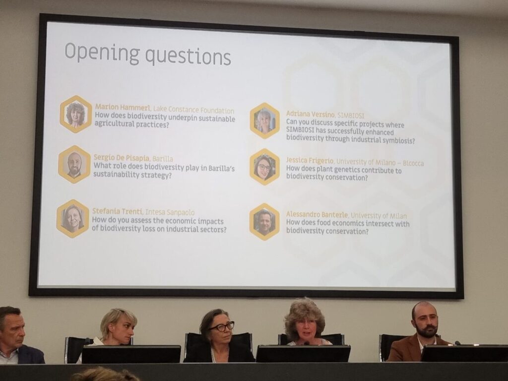 Zusehen sind die Teilnehmer*innen der Podiumsdiskussion. Sie sitzen auf Stühlen hinter einem langen Pult. Auf der Präsentation hinter ihnen sind "opening questions" dargestellt. Marion Hammerls Frage ist: "How does biodiversity underpin sustainable agricultural practices?"