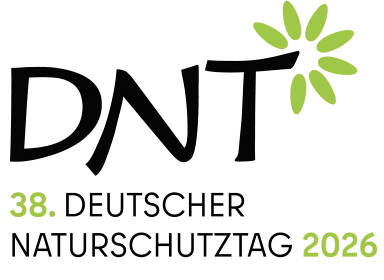 Im Blick ist das Logo des DNT. Um das „T“ ist oben rechts eine abstrakte Blume mit sieben Blütenblättern angeordnet. Unter den drei Buchstaben DNT steht der Schriftzug „38. Deutscher Naturschutztag 2026“. Die Zahlen 38 und 2026 sind im gleichen Grünton gehalten wie die Blume.