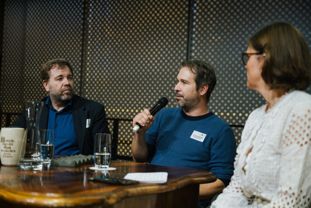 Drei Personen sitzen um den Stammtisch und diskutieren.