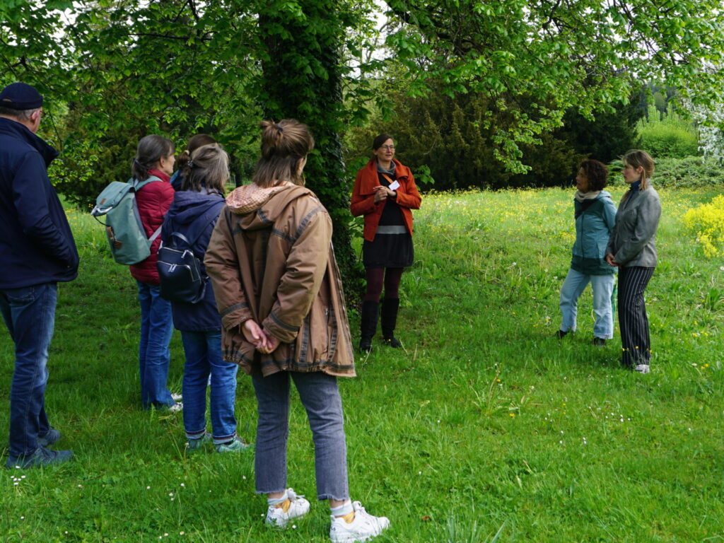 Die Teilnehmer*innen stehen unter einem grünen Baum. Daniela Dietsche erzählt ihnen von den umgesetzten Klimawandelanpassungsmaßnahmen der Stiftung Liebenau.