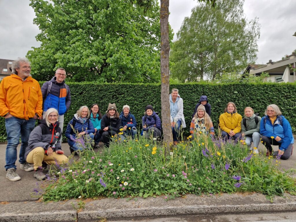 Zu sehen ist ein Gruppenbild der Teilnehmer*innen der Exkursion. Sie knien um ein Trittsteinbiotop von blühenden Blumen.