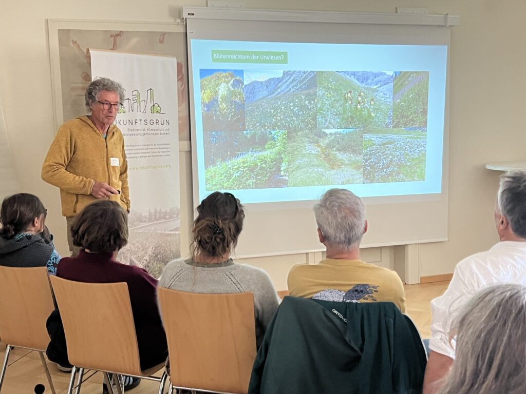 Hauptredner Alfred Karle-Fendt steht vor seinen Präsentationsfolien. Vor ihm sitzen Teilnehmer*innen, die gespannt zuhören.