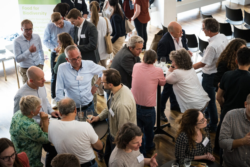 Blick aus der Vogelperspektive: Konferenzteilnehmer*innen stehen an Stehtischen zusammen und unterhalten sich.