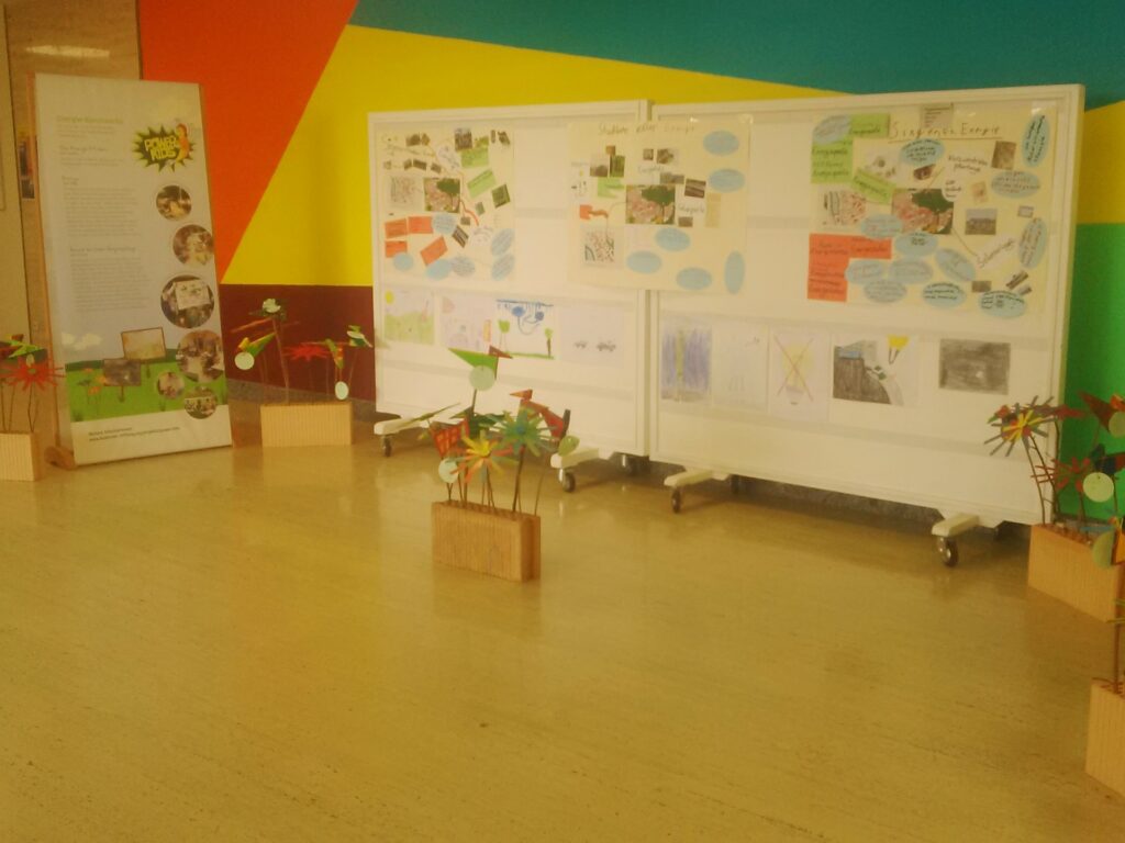 Blick auf eine Ausstellung: Auf großen Pinwänden sind viele kleine Elemente angebracht. Links steht ein Roll-up.