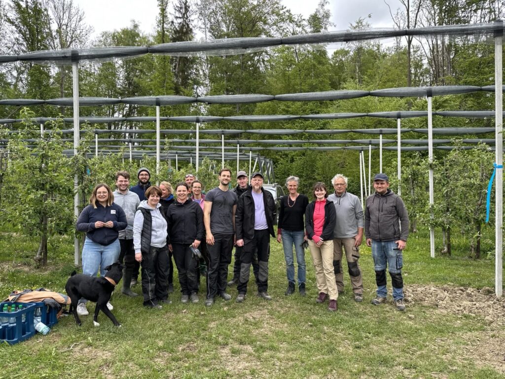 Eine Gruppe von 15 Menschen steht vor einer Obstanlage und schaut in die Kamera.