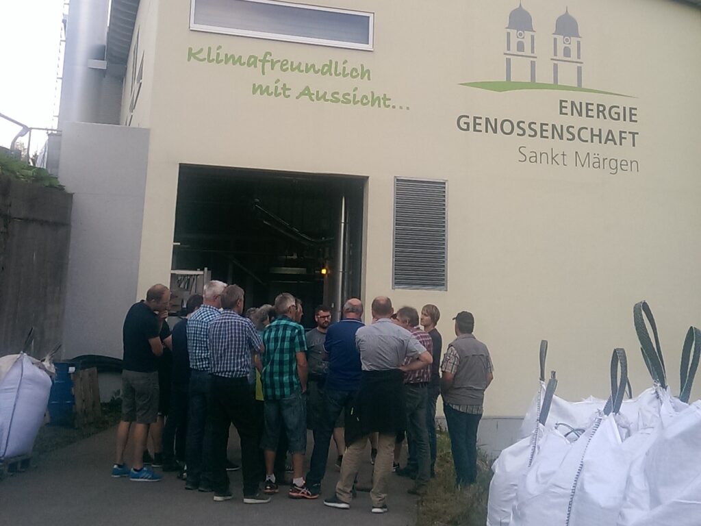 Eine Gruppe von Menschen steht vor dem Eingang der Energiegenossenschaft von Sankt Märgen. Auf der Fassade steht "klimafreundlich mit Aussicht".