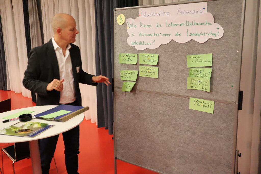 Ein Mann steht links von einer Pinwand und bringt Notizen an.