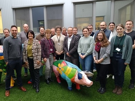 18 Menschen stehten hinter einer bunt angemalten Schweine-Figur.