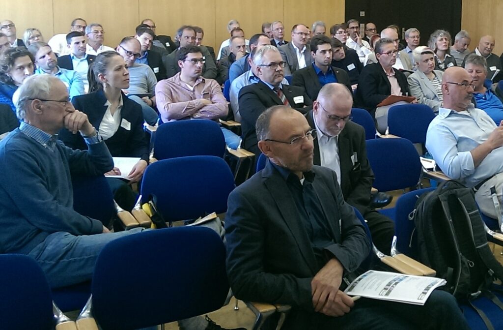 Blick in das Publikum einer Konferenz, das in Kinobestuhlung sitzt und nach vorne schaut.