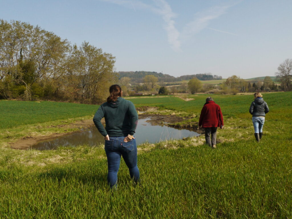 Drei Frauen sind von hinten zu sehen. sie gehen zu einem Kleingewässer, das vor ihnen liegt.