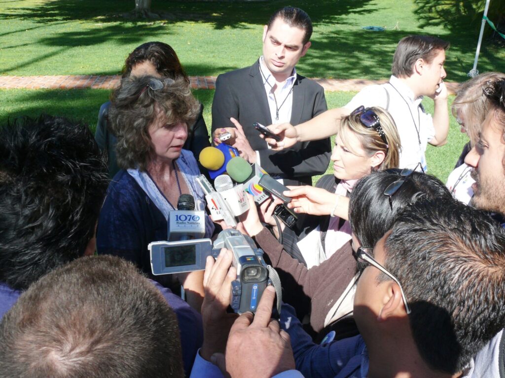 Marion Hammerl steht im Zentrum des Bilds. Um sie drängen sich Journlastinnen und Journalisten, die ihr Mikrofone hinhalten.