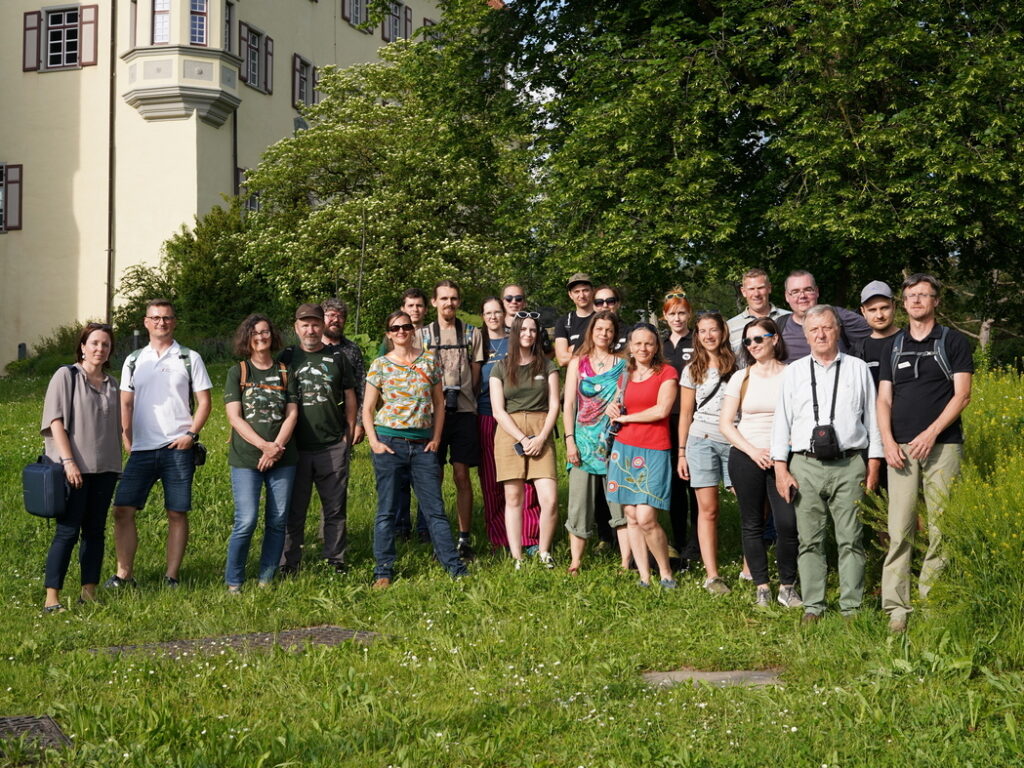 Eine Gruppe von rund 20 menschen steht auf einer Wiese und blickt in die Kamera.