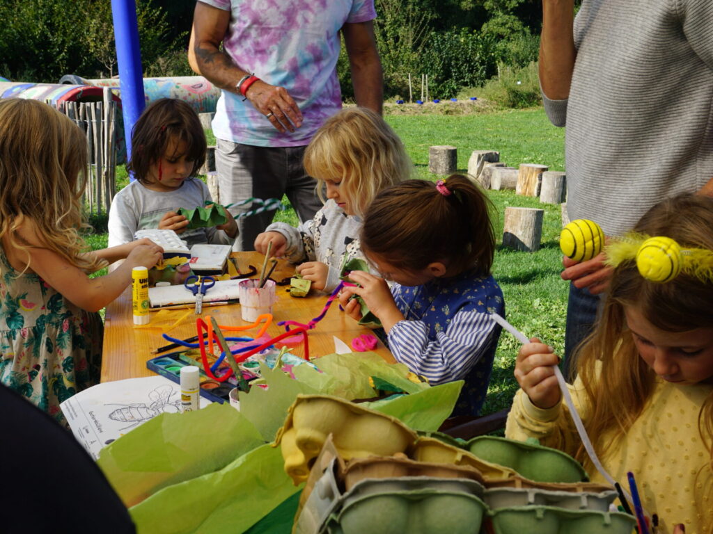 Blick auf bastelnde Kinder, die im Freien an einem Tisch sitzen