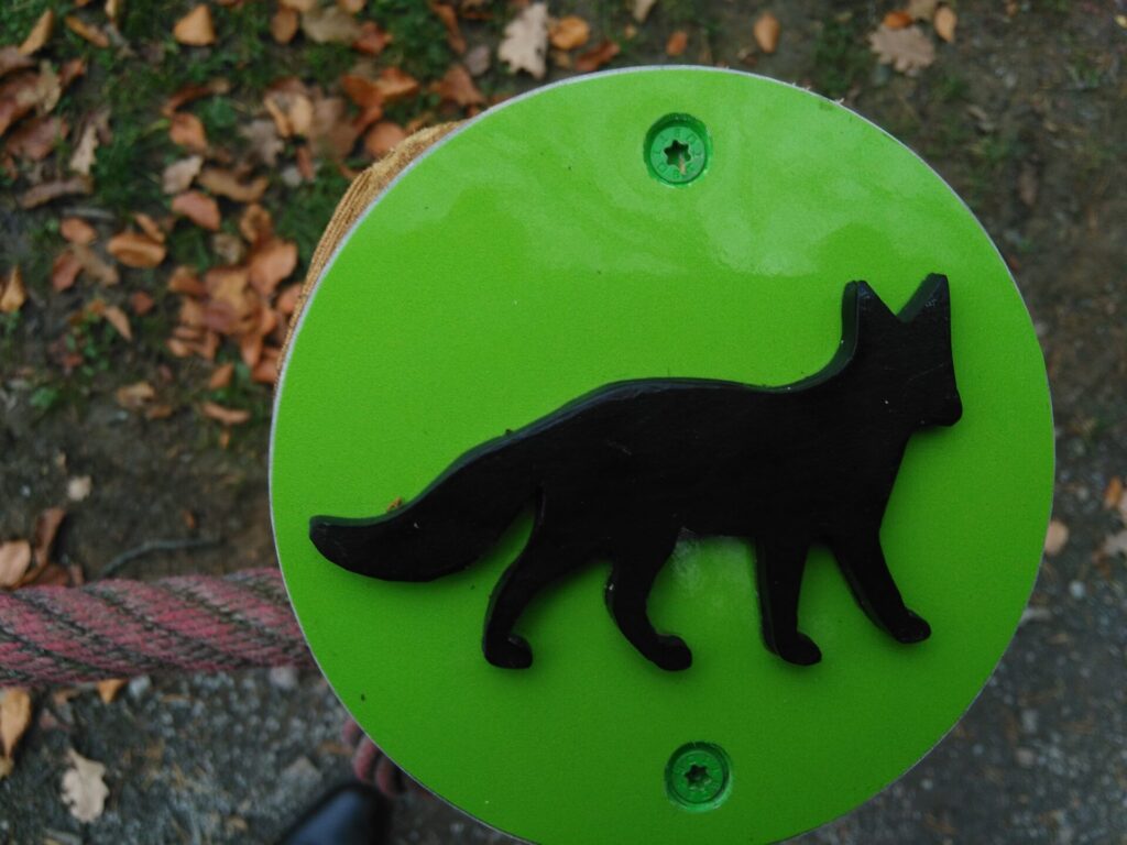 Auf einer grünen Plakette ist ein schwarzer Fuchs zu sehen. Er hebt sich von der Plakette ab und ist zu ertasten.