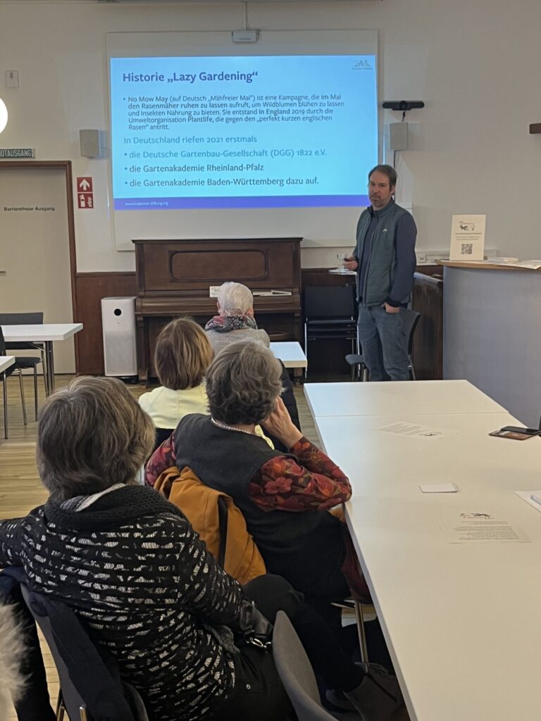 Dr. Immanuel Schäfer steht vor seinen Präsentationsfolien. Vor ihm sind 4 Teilnehmende zu sehen.