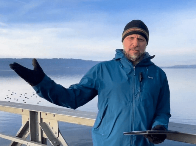 Zusehen ist Geschäftsführer der Bodensee-Stiftung Volker Kromrey, der auf einem Steg steht und mit seiner rechten Hand gestikuliert. Im Hintergrund sieht man einen See.
