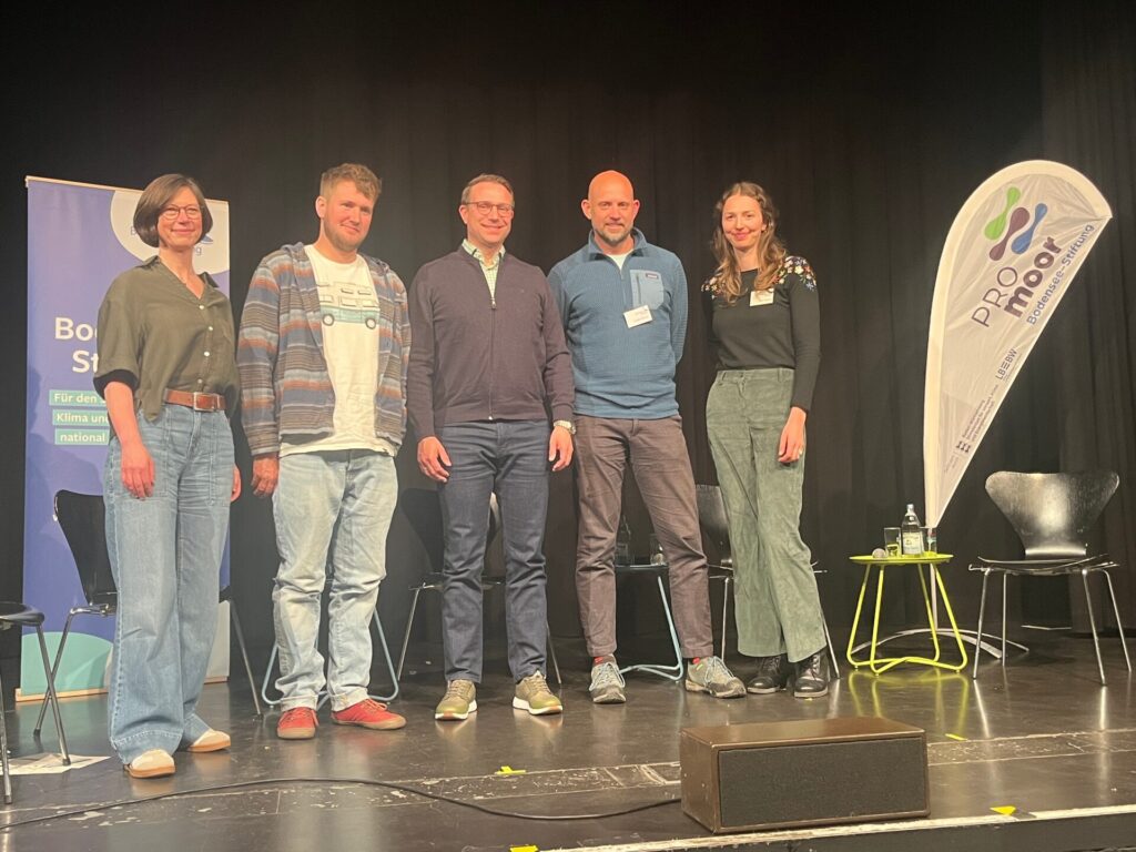 Fünf Mensche stehen auf einer Bühne vor einem Roll-Up der Bodensee-Stiftung und einer Beachflag mit dem Logo PROmoor
