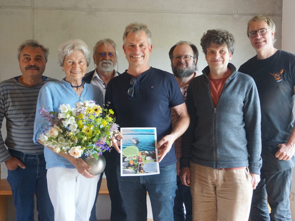 Zu sehen sind die genannten Personen stehend nebeneinander. Hildegard Breiner und Jörg Dürr-Pucher stehen in der vorderen Reihe. Sie hält einen Blumenstrauß in der Hand.