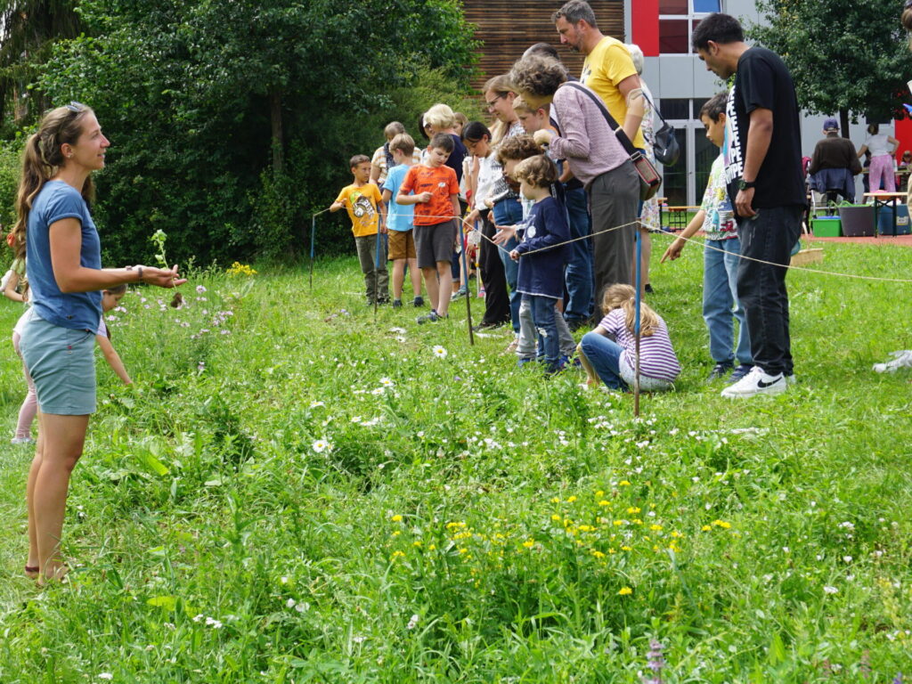 Zu sehen ist Saskia Wolf, die den Eltern die heimischen Wildblumen vorstellt, die auf der Blühwiese blühen.