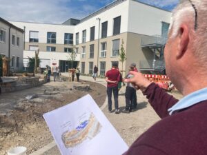 Auf dem Bild zeigt Landschaftsplaner Thomas Wuttke auf die Anlage und hält ein Blattpapier mit dem Plan in der Hand.