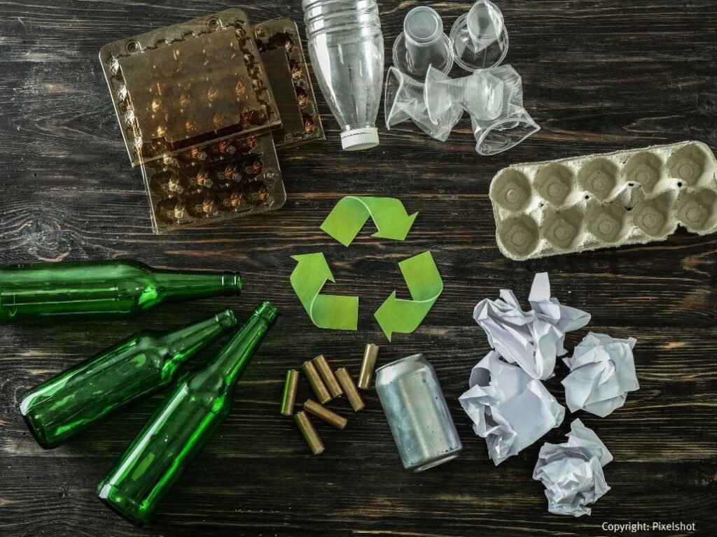 Verschiedene Verpackungen liegen kreisförmig um das grüne Recyclingzeichen.