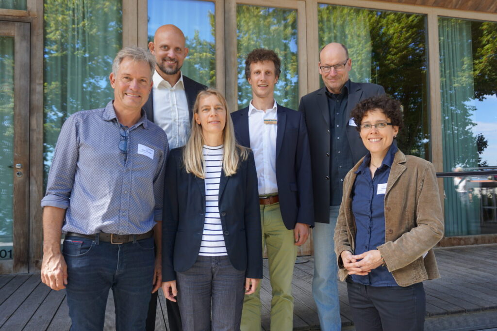 Sechs Personen des Organisationsteams posieren für ein Gruppenfoto vor einer Glasfassade.