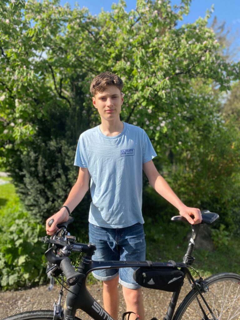 Auf dem Bild ist Leon mit seinem Fahrrad zu sehen. Er steht vor einer Hecke.