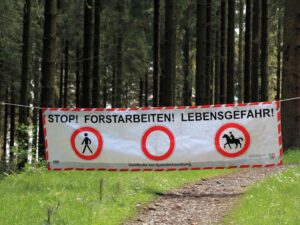 Auf dem Bild ist ein großer Banner zusehen, der zwischen zwei Bäumen gespannt wurde. Darauf steht "STOP! Forstarbeiten! Lebensgefahr!