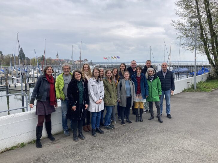 Die Gruppe steht vor einem Hafen für Segelboote und schaut in die Kamera.