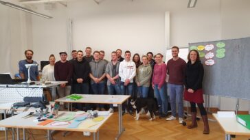 Die Gruppe steht neben einer Pinnwand für ein Gruppenbild.