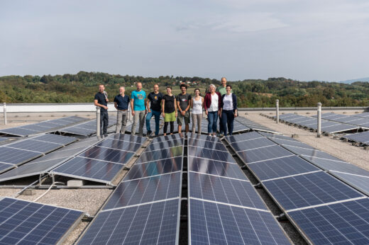 Sehr viele Solarmodule sind auf einem Dach befestigt. Eine Menschengruppe steht zwischen den Panelen.