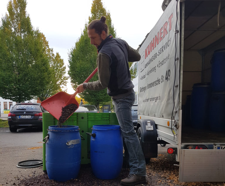 Ein Mann leert Restmasse mithilfe einer Schaufel in große blaue Plastik Behälter.