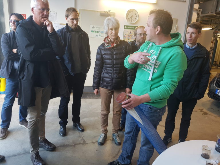 7 sieben Personen stehen um einen Tisch mit Wasserproben. Ein Mann erklärt der Gruppe was darüber.