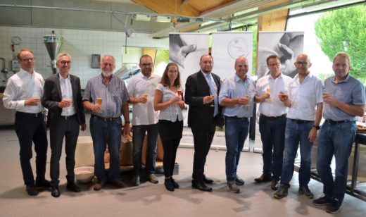Zehn Personen stehen in Reihe für ein Gruppenbild mit Getränke in der Hand.