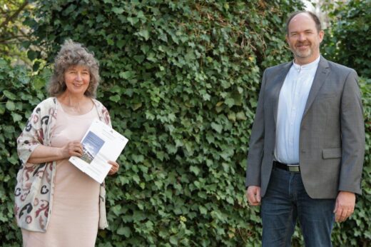 Zwei Personen stehen vor einer Hecke. Die Frau links hat das Kooperationspapier in der Hand.