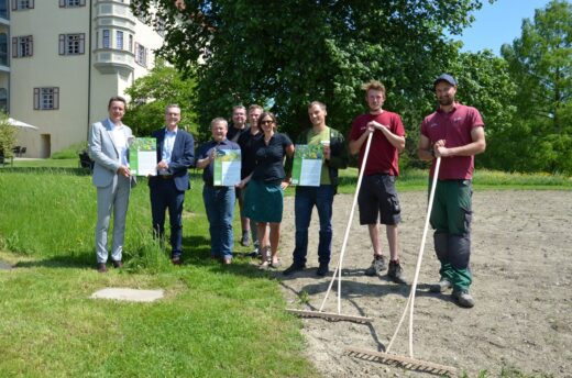 Neun Personen stehen auf dem Firmengelände der Stiftung Liebenau. Die zwei Personen von rechts halten einen Rechen in der Hand.