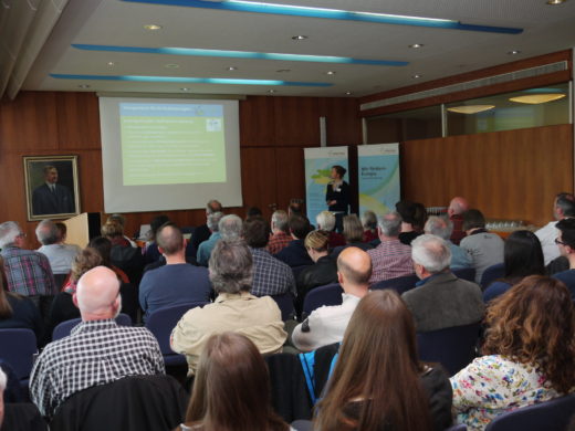 Eine Referentin steht vor einer Leinwand mit Präsentation und spricht zu einem vollbesetzten Saal mit rund 50 Teilnehmenden. Im Hintergrund ist ein Roll-up der Bodensee-Stiftung zu sehen.