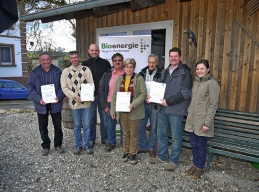 Auszeichnung von Biogasbetrieben durch die Bodensee-Stiftung: Acht Personen stehen vor einem Holzgebäude mit dem Banner „Bioenergie Region Bodensee". Mehrere Teilnehmende halten Zertifikate in den Händen.