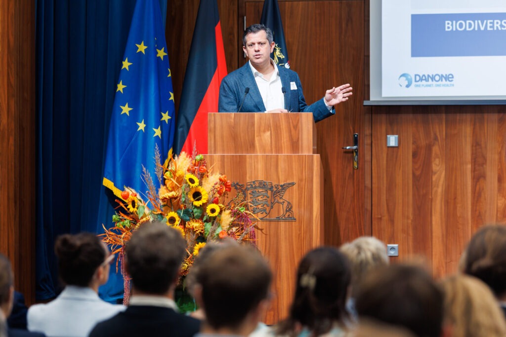 Ein Mann steht vor einer Europaflagge in einem Konferenzsaal an einem Rednerpult.