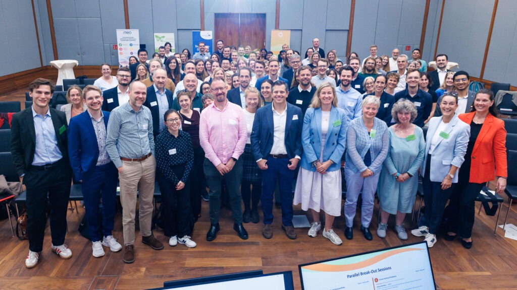 Blick in einen Konferenzsaal. Mehr als 100 Menschen stehen in einer Gruppe und blicken in die Kamera.
