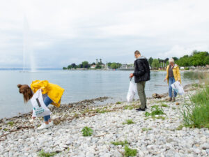 Ein Mann und zwei Frauen sammeln am Bodenseeufer Müll auf.