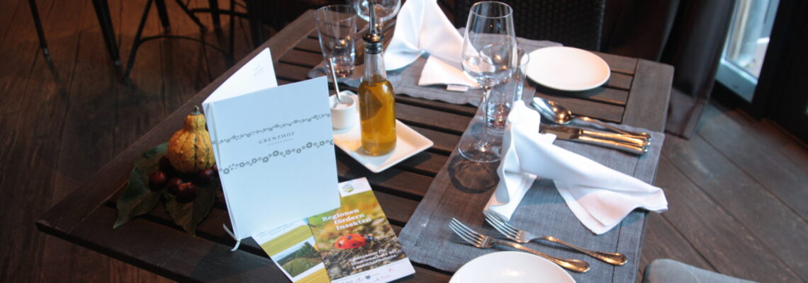 Blick auf einen gedeckten Tisch mit Menükarte vom Restaurant Grenzhof