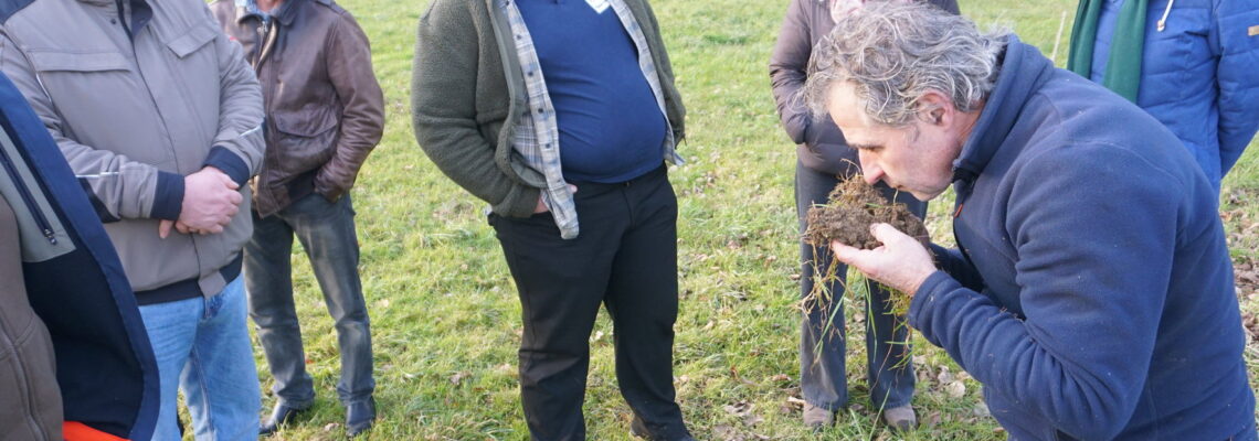 Eine Gruppe von sechs Menschen steht um einen Mann, der Boden in Händen hält und vorgebeugt daran riecht.