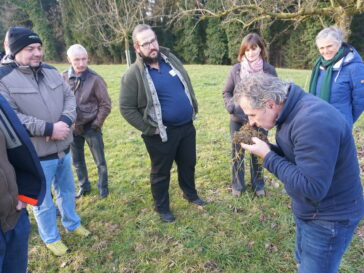 Eine Gruppe von sechs Menschen steht um einen Mann, der Boden in Händen hält und vorgebeugt daran riecht.