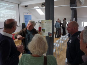 In einem Tagungsraum stehen miteinander diskutierend zwei Gruppen jeweils um Pfosten, an denen Poster hängen.