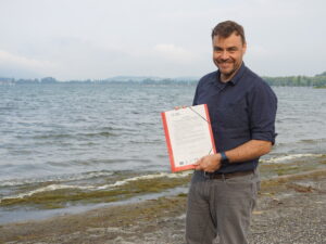 Dimitri Vedel steht am Bodenseeufer und hält das Seenpapier in der Hand