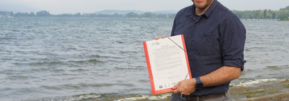 Dimitri Vedel steht am Bodenseeufer und hält das Seenpapier in der Hand