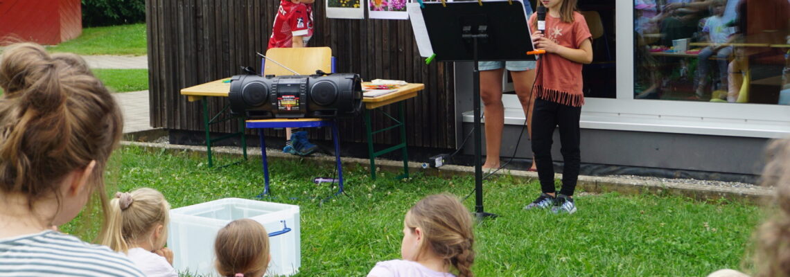 Vor einer Gruppe von Schülern und Eltern präsentieren eine Schülerin und ein Schüler, unterstützt von Saskia Wolf.
